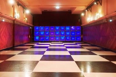 Hall d'entrée avec murs aux formes ondulées, sol à motifs géométriques et escalier menant à une porte noire.