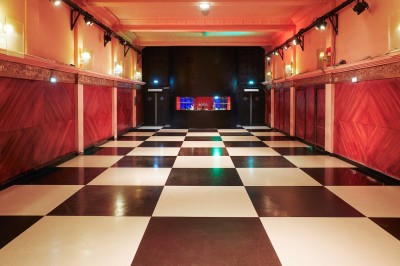 Hall d'entrée avec murs aux formes ondulées, sol à motifs géométriques et escalier menant à une porte noire.