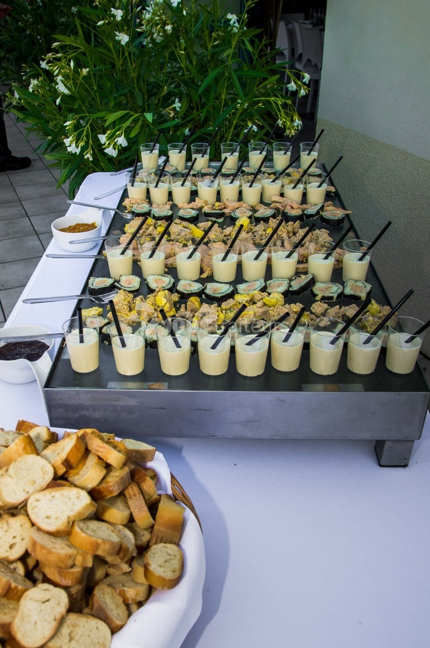 Buffet de verrines salées accompagnées de croûtons, disposé sur une table en extérieur avec des plantes en arrière-plan.