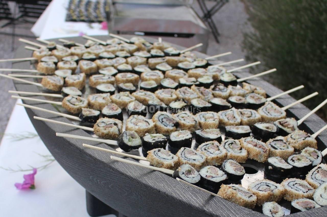 Plateau en bois rempli de brochettes de sushis variés, disposé sur une table en extérieur.