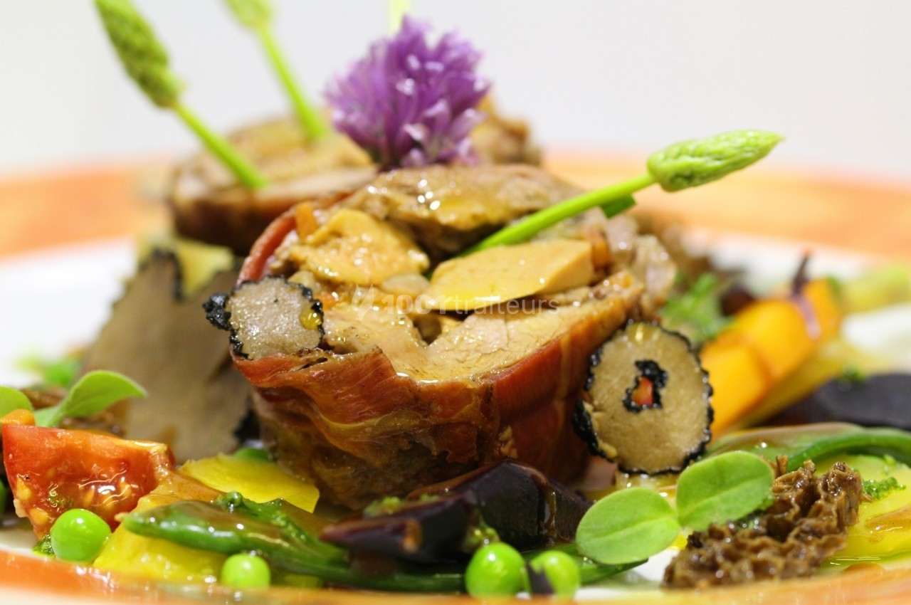 Plat gastronomique composé de viande, légumes colorés, truffes et asperges, présenté avec soin sur une assiette.