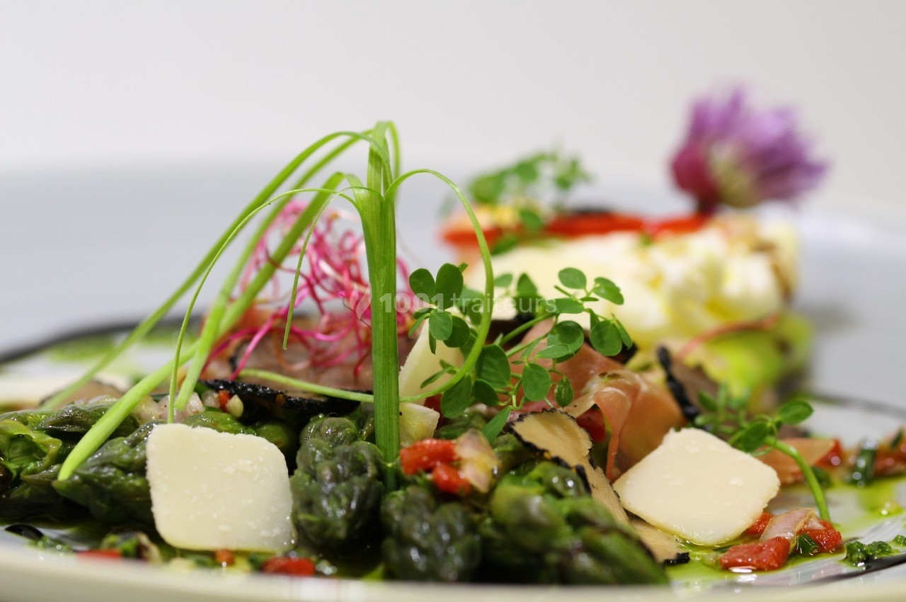Assiette garnie d'asperges, copeaux de fromage, truffes et herbes fraîches, avec une présentation soignée.