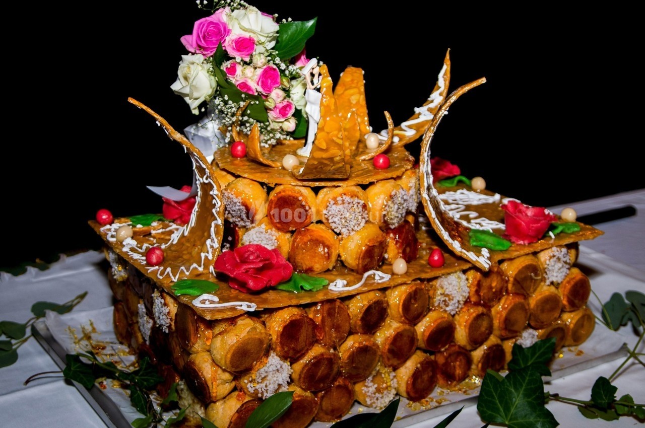 Pièce montée en choux garnie de décorations en sucre, fleurs roses et feuilles vertes sur une table blanche.