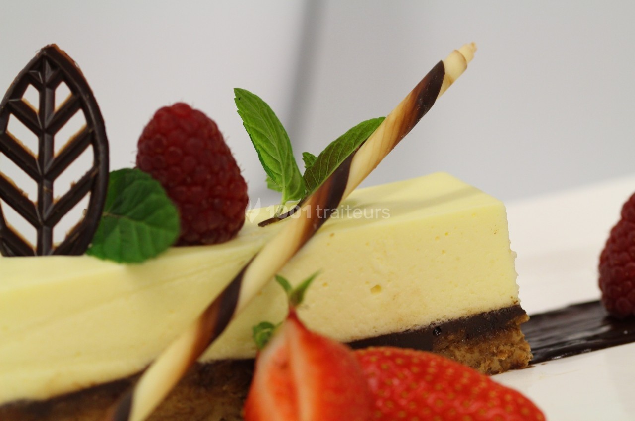 Part de gâteau au citron surmontée de framboises, fraises, feuille de chocolat et décor en biscuit torsadé.