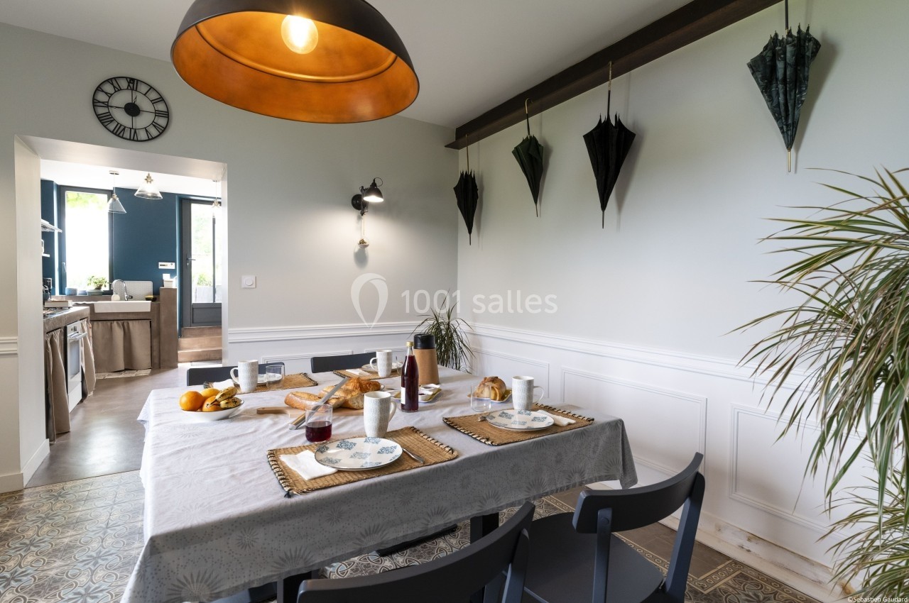 Salle à manger lumineuse avec table dressée pour le petit-déjeuner, décorée de parapluies suspendus au mur.