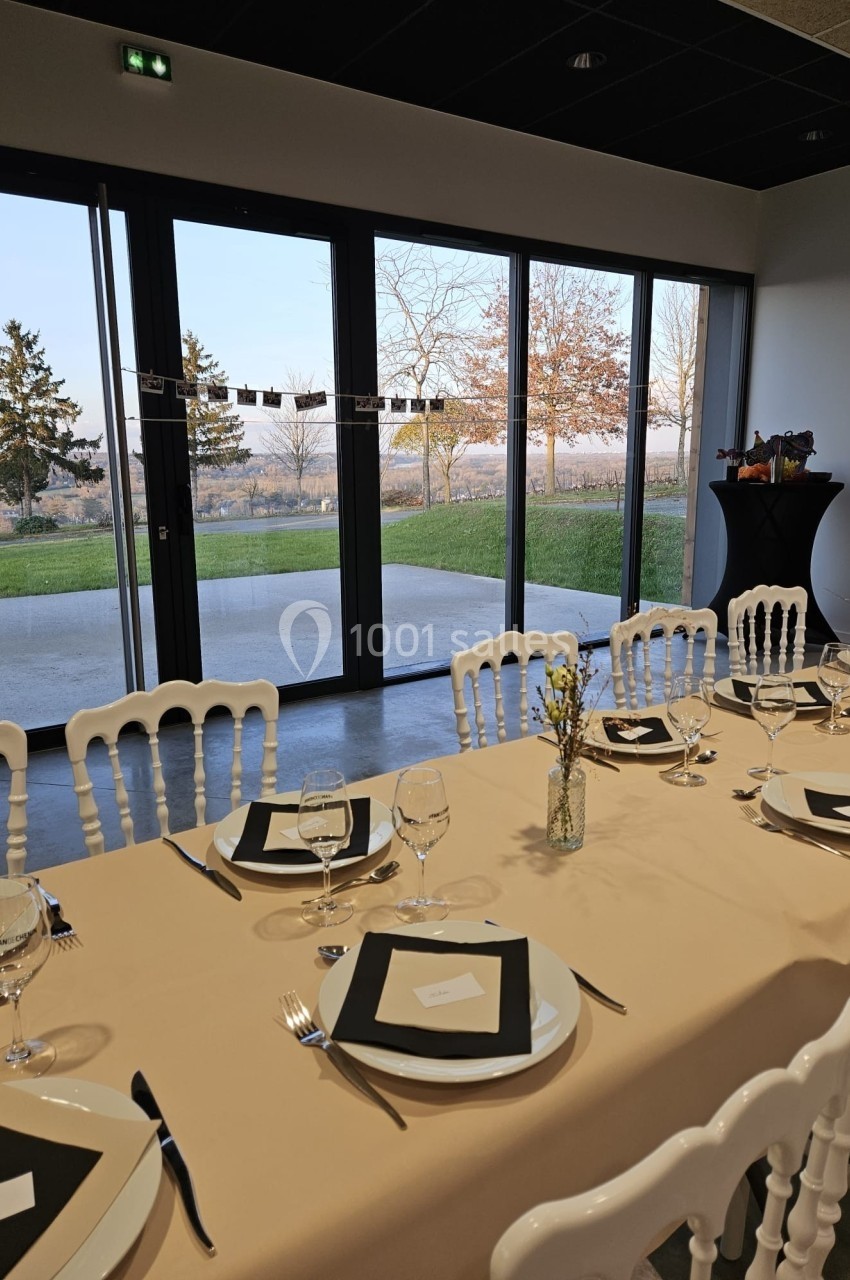 Table dressée avec nappes beiges, assiettes et verres, près de grandes baies vitrées donnant sur un jardin.