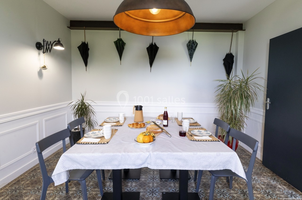 Salle à manger avec table dressée pour quatre personnes, décorée de plantes et de parapluies accrochés au mur.