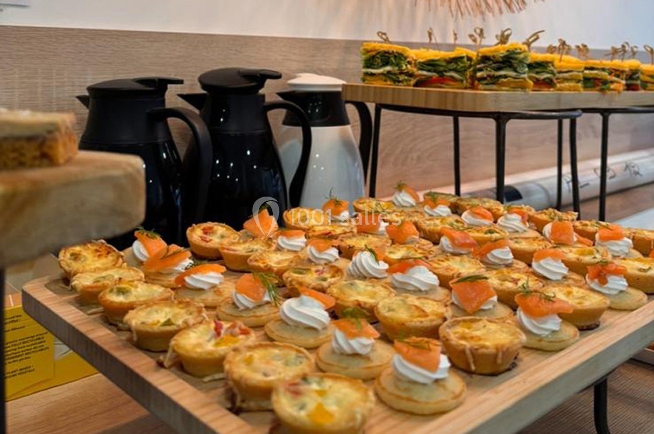 Plateau de mini-quiches et bouchées salées avec carafes en arrière-plan sur une table en bois.