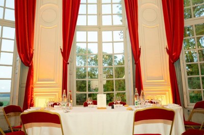 Table ronde dressée pour un repas, avec nappes blanches, couverts, verres, pains et centre de table floral.