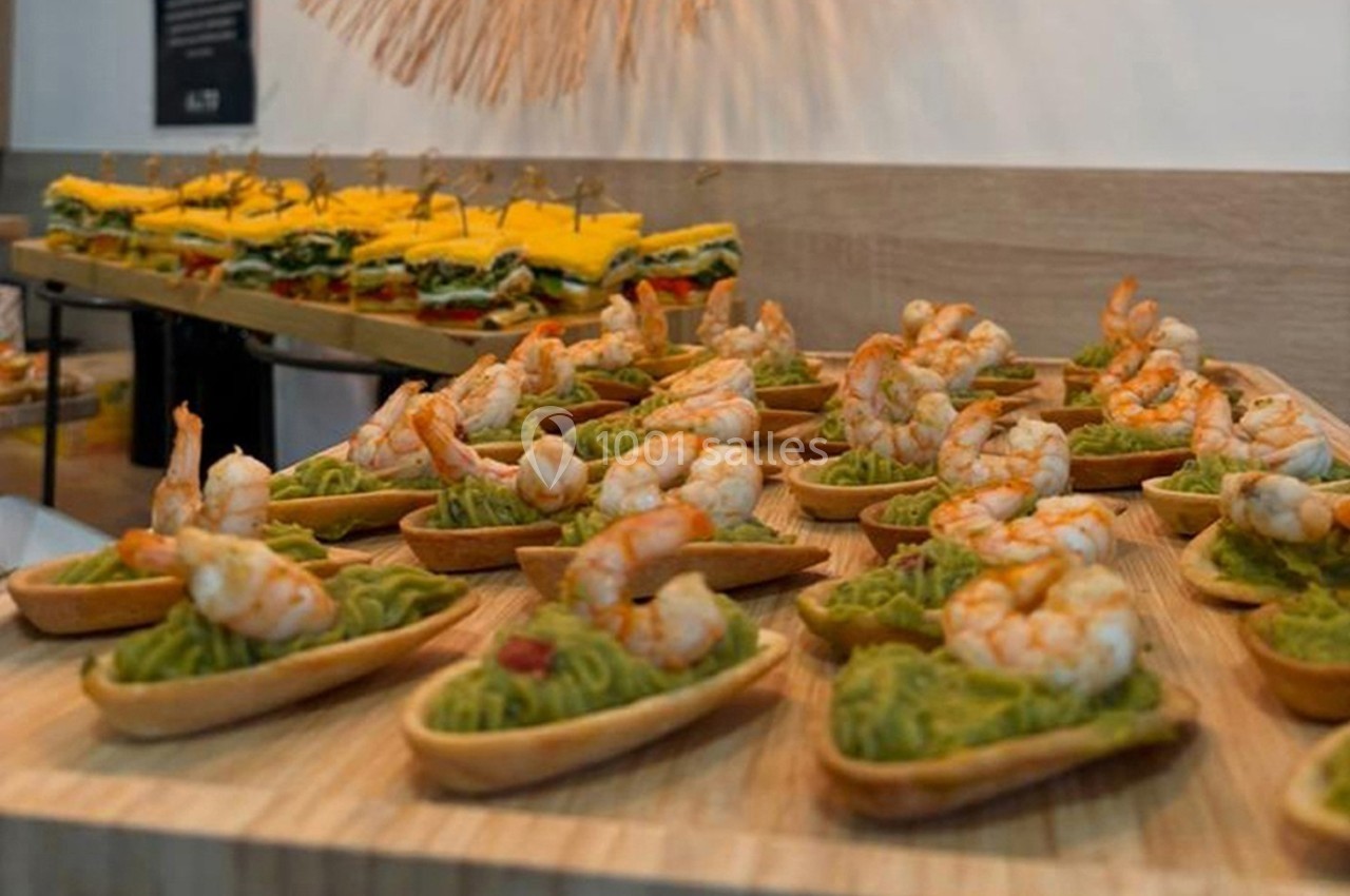 Tartelettes garnies de guacamole et crevettes, disposées sur un plateau en bois, avec des amuse-bouches en arrière-plan.