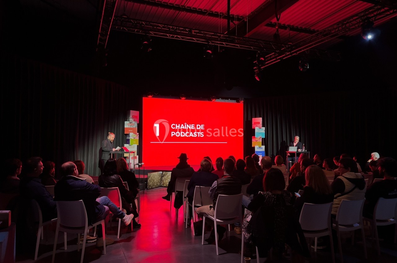 Présentation sur scène devant un public, avec un écran rouge affichant ’Chaîne de podcasts’ en grand.