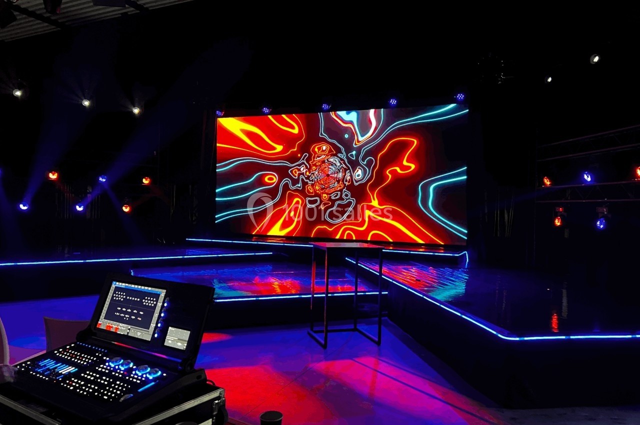 Scène illuminée avec écran LED affichant des motifs colorés abstraits, console de contrôle au premier plan.