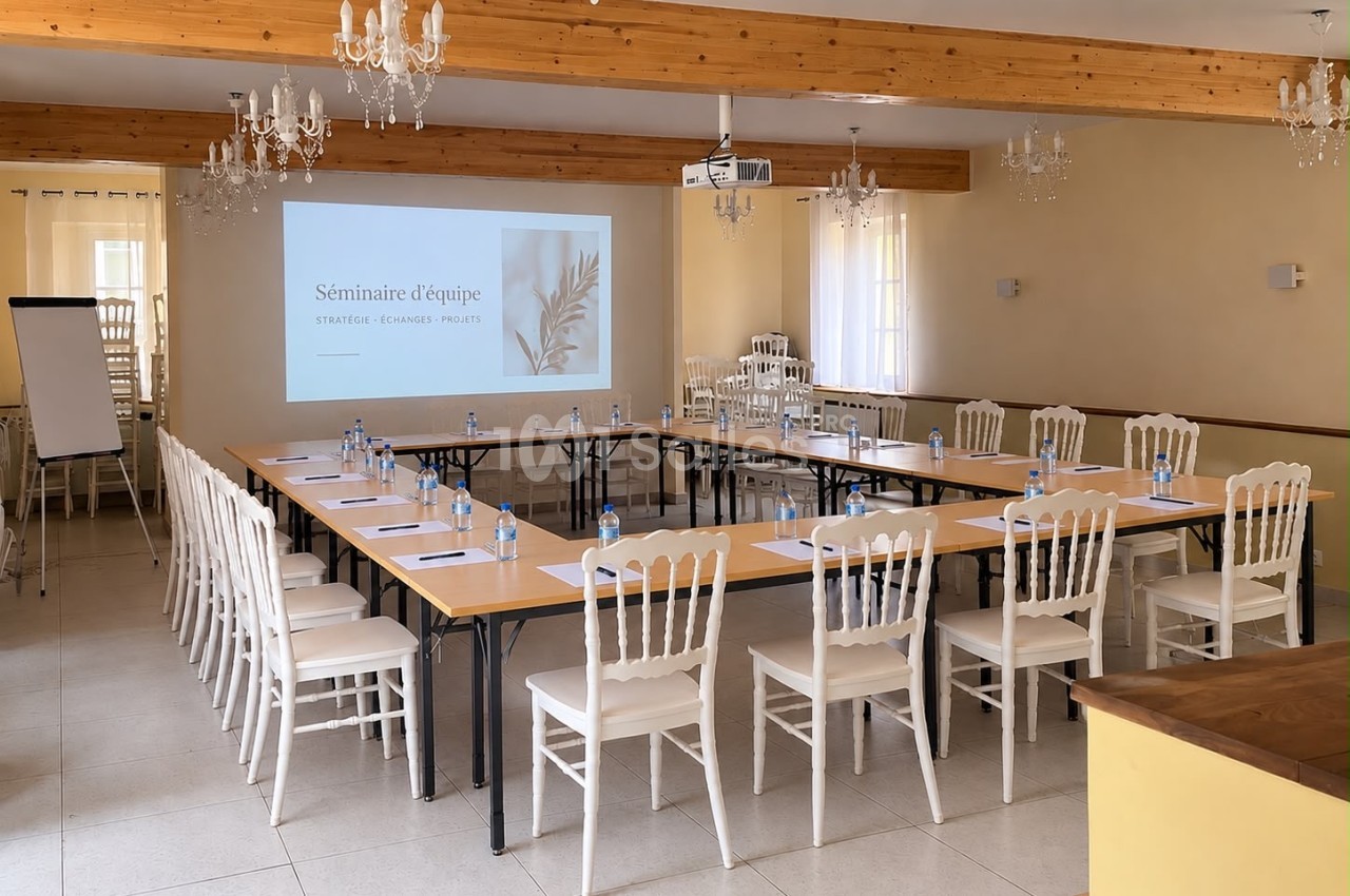 Salle de réunion aménagée en U avec chaises blanches, face à un écran de projection, sous poutres apparentes.