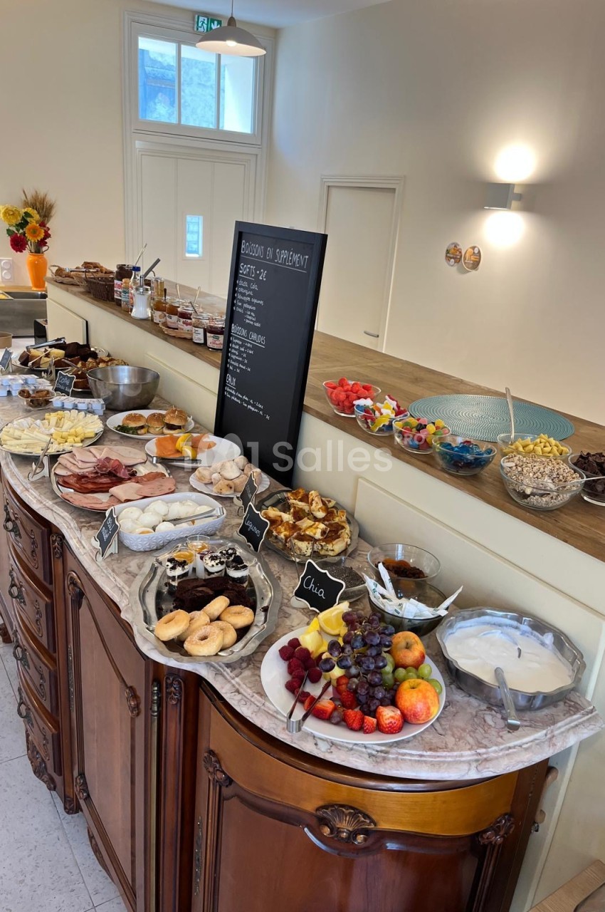 Buffet de petit-déjeuner dressé sur un meuble ancien en bois et marbre : viennoiseries, charcuteries, fromages, fruits frais, yaourts et coupelles de céréales.