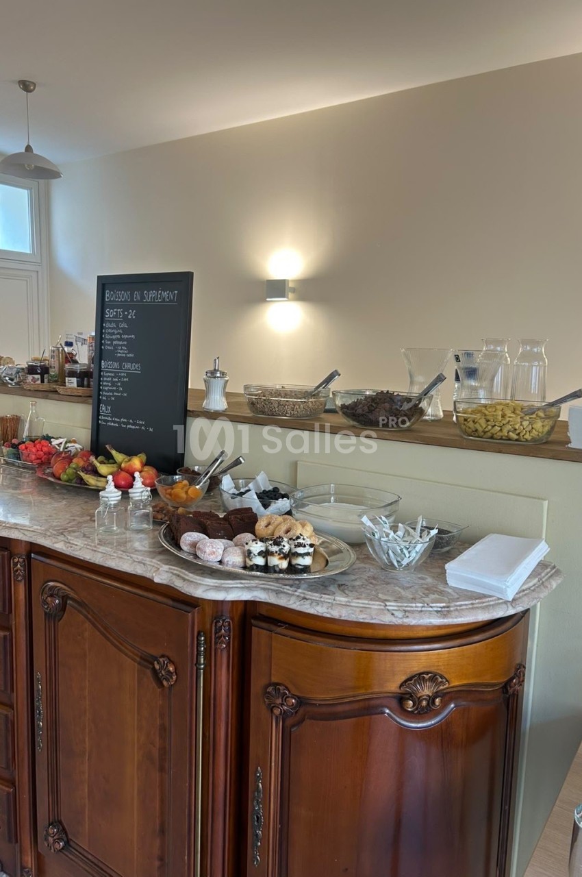 Buffet de pâtisseries, de fruits et de céréales en coupelles sur un meuble ancien en bois au plateau de marbre.