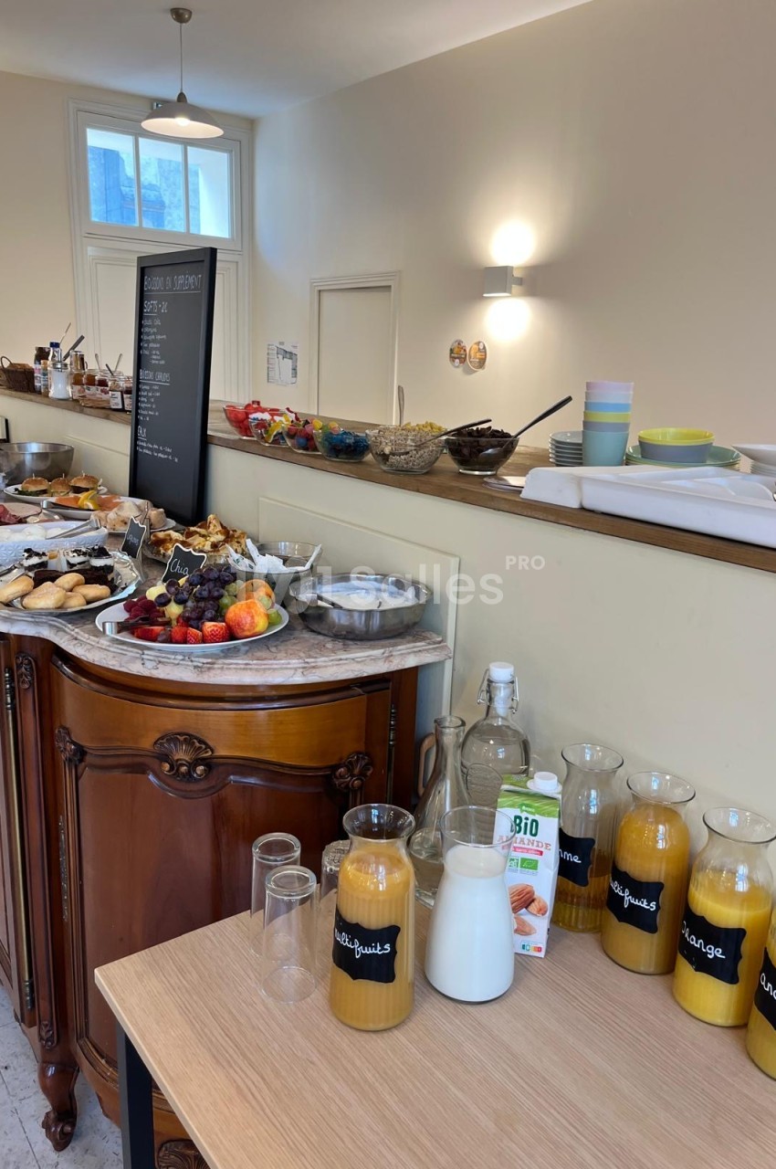 Buffet de petit-déjeuner : viennoiseries, fruits frais, céréales et carafes de jus sur un meuble en bois.
