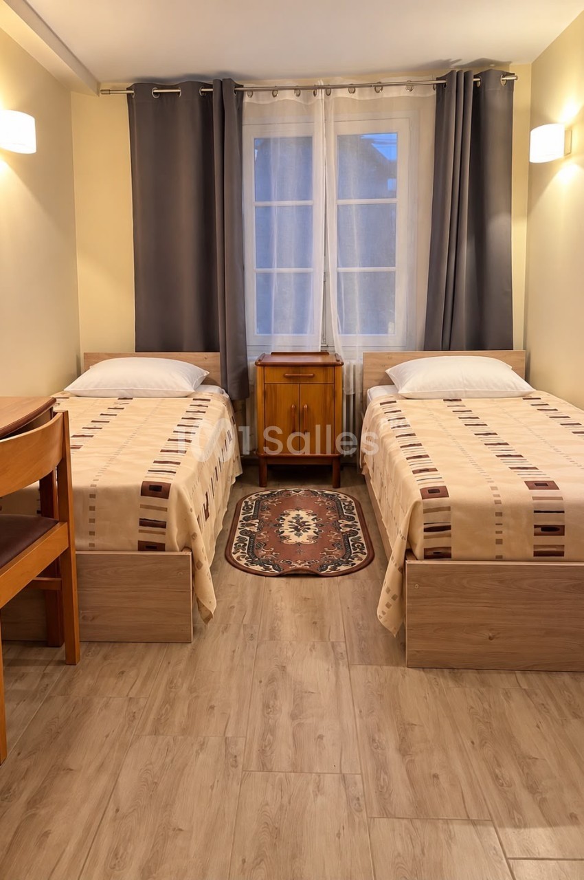 Chambre à deux lits simples jumeaux recouverts de dessus-de-lit beige, séparés par une table de chevet en bois et un petit tapis, éclairée par des appliques murales.