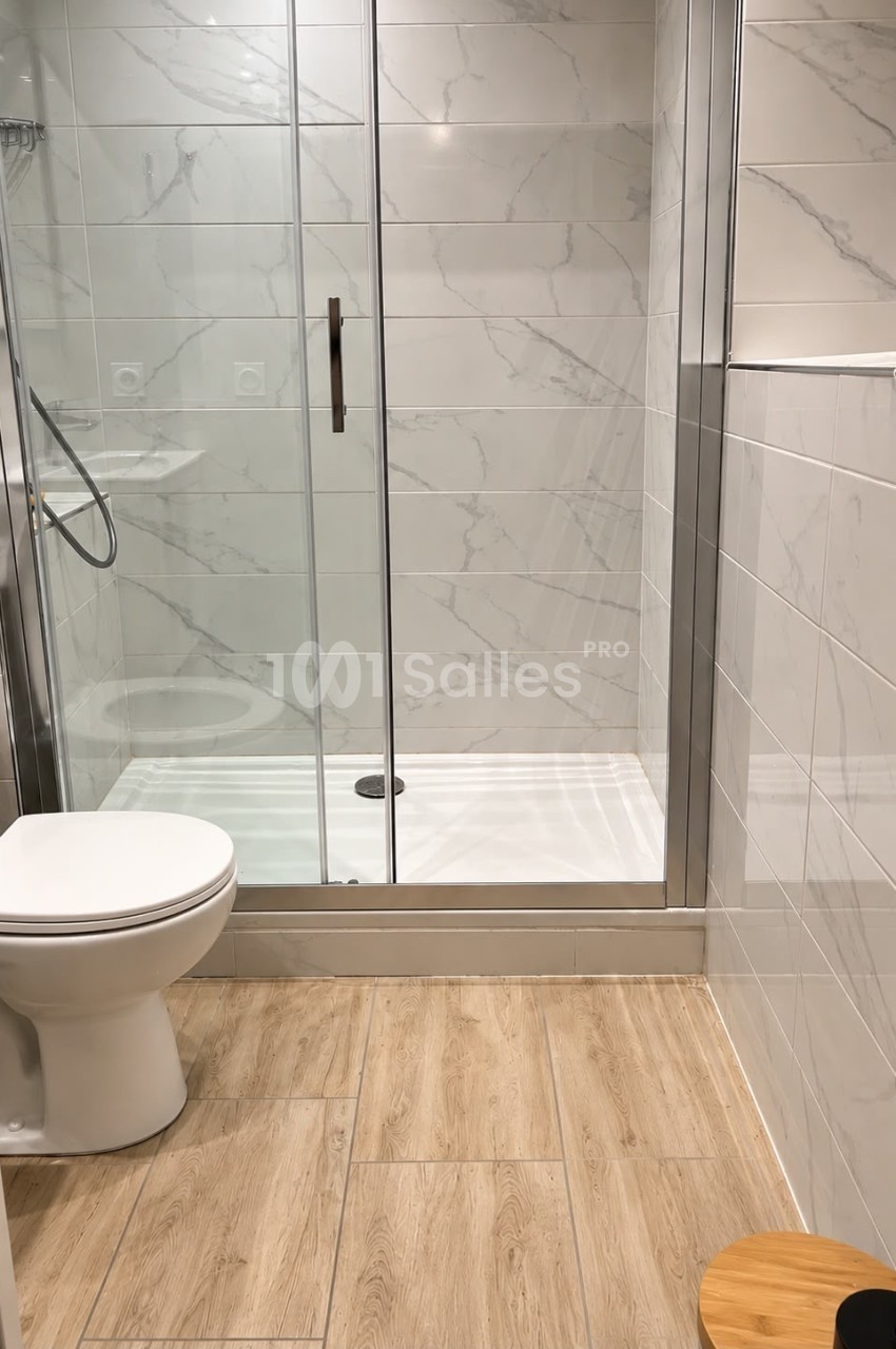 Douche à l'italienne aux parois vitrées et carrelage imitation marbre blanc, à côté de toilettes, sur un sol en lames de bois clair.