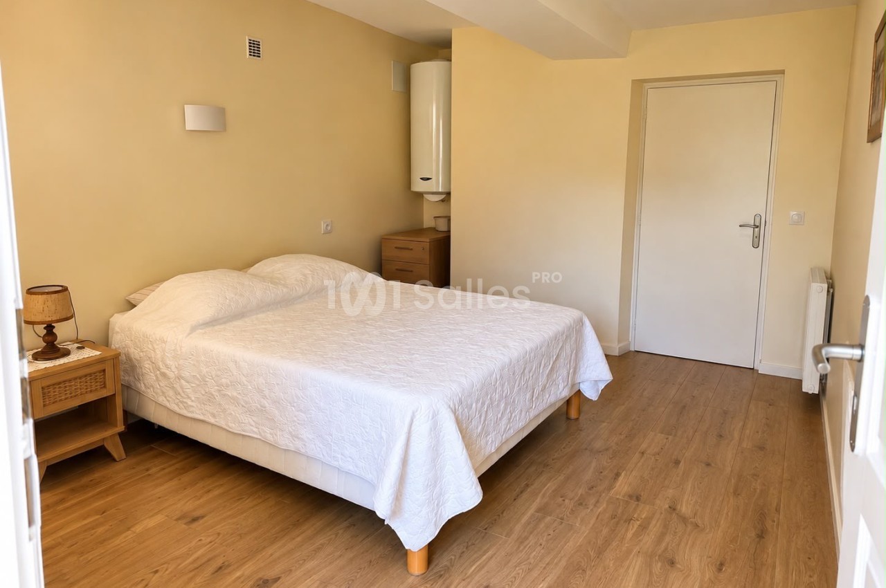 Chambre à coucher avec un grand lit recouvert d'un dessus de lit blanc matelassé, une table de chevet en bois et un parquet clair.