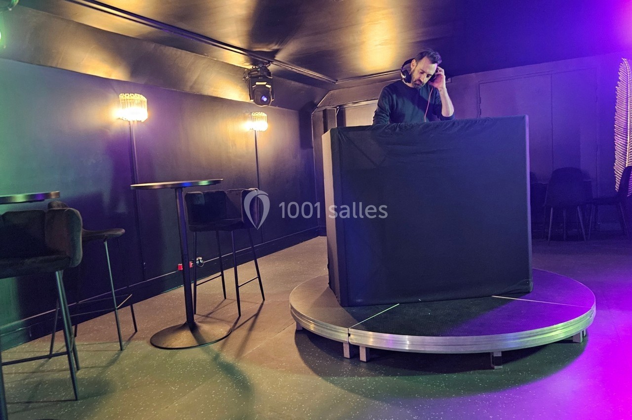 Un DJ mixe sur une scène circulaire dans une salle sombre éclairée par des lumières colorées.