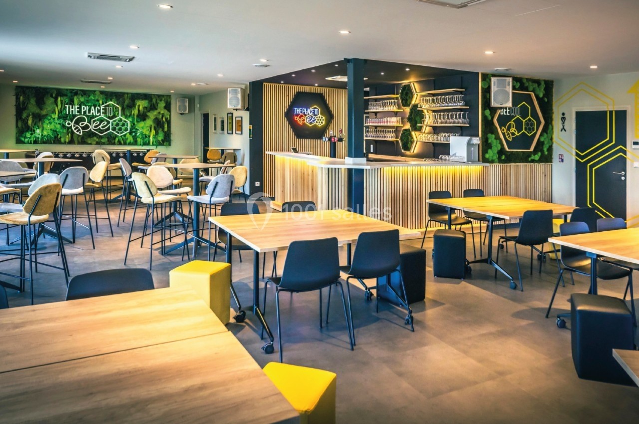 Salle de restauration moderne avec tables en bois, chaises variées et décoration murale sur le thème des abeilles.