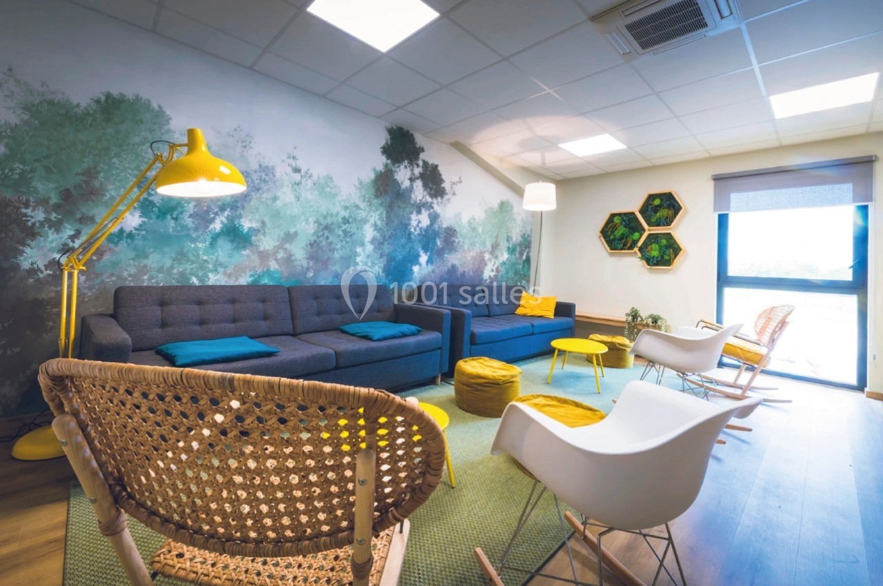 Espace salon lumineux avec canapés bleus, fauteuils design, lampadaire jaune et mur décoré d'une fresque végétale.