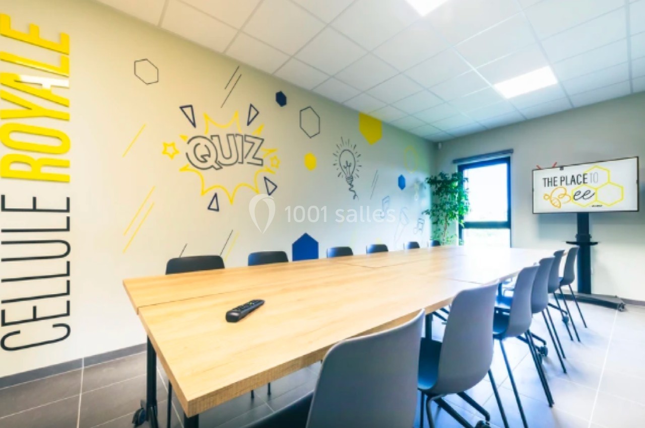 Salle de réunion lumineuse avec une grande table, des chaises, un écran affichant ’The Place to Bee’ et des décorations…