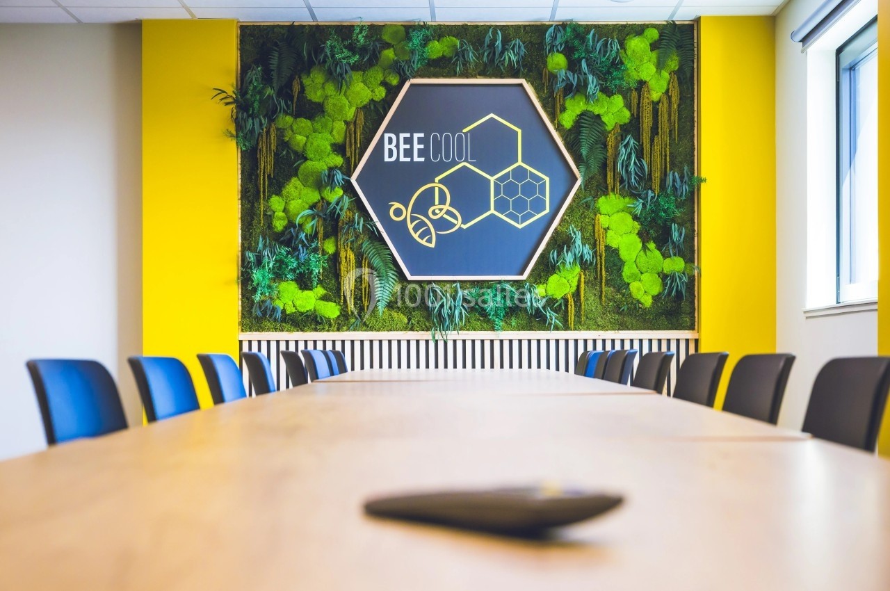 Salle de réunion avec table en bois, chaises noires et mur végétal décoré d'un panneau hexagonal ’Bee Cool’.