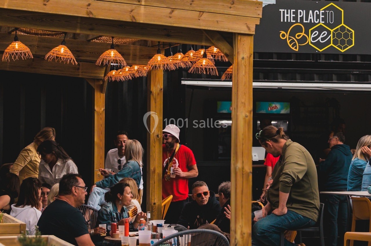 Groupe de personnes discutant et partageant un repas en terrasse sous un éclairage chaleureux.