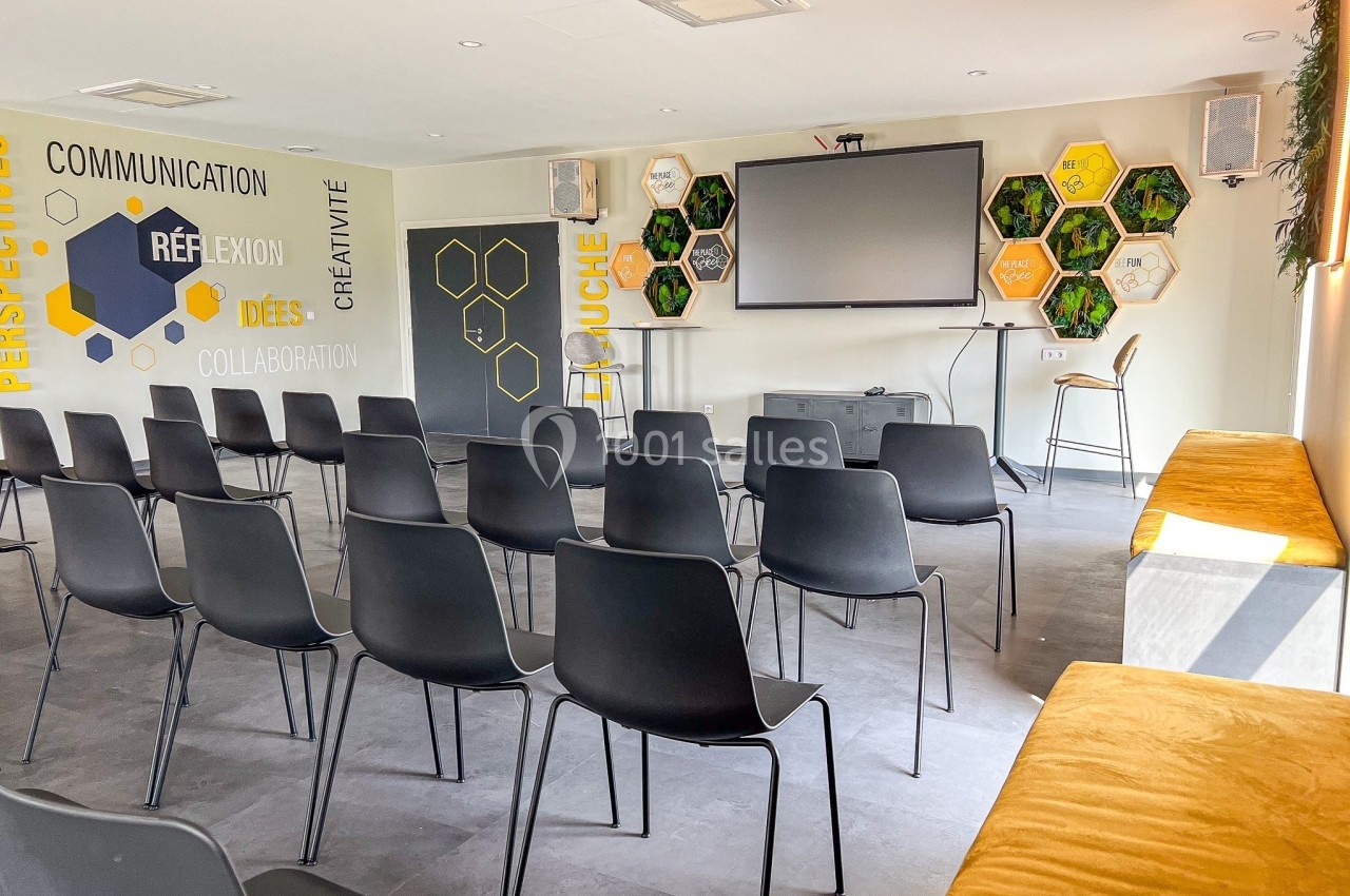 Salle de réunion lumineuse avec chaises noires alignées, écran de projection et décorations murales hexagonales colorées.