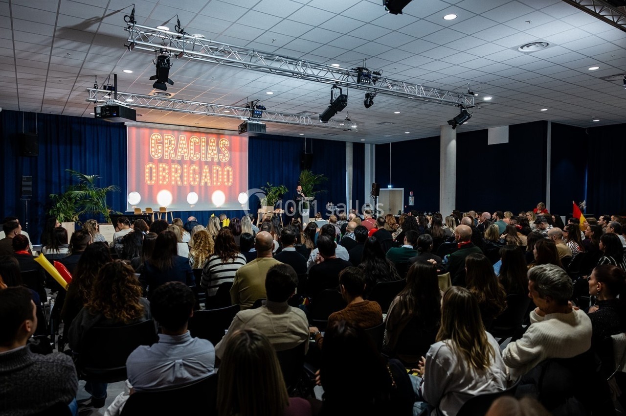 Salle remplie de personnes assistant à un événement avec une scène illuminée affichant ’Gracias Obrigado’.