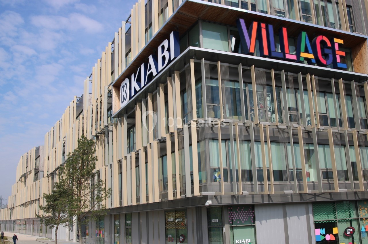 Façade moderne d'un centre commercial avec enseignes colorées, dont ’Kiabi’ et ’Village’, sous un ciel partiellement nuageux.
