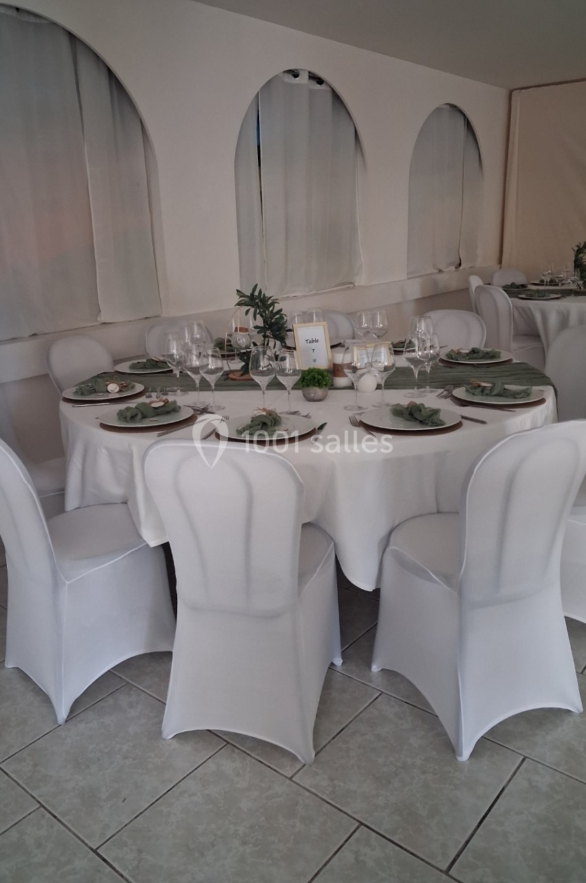 Table ronde élégamment dressée avec nappes blanches, vaisselle raffinée et décorations végétales, entourée de chaises…