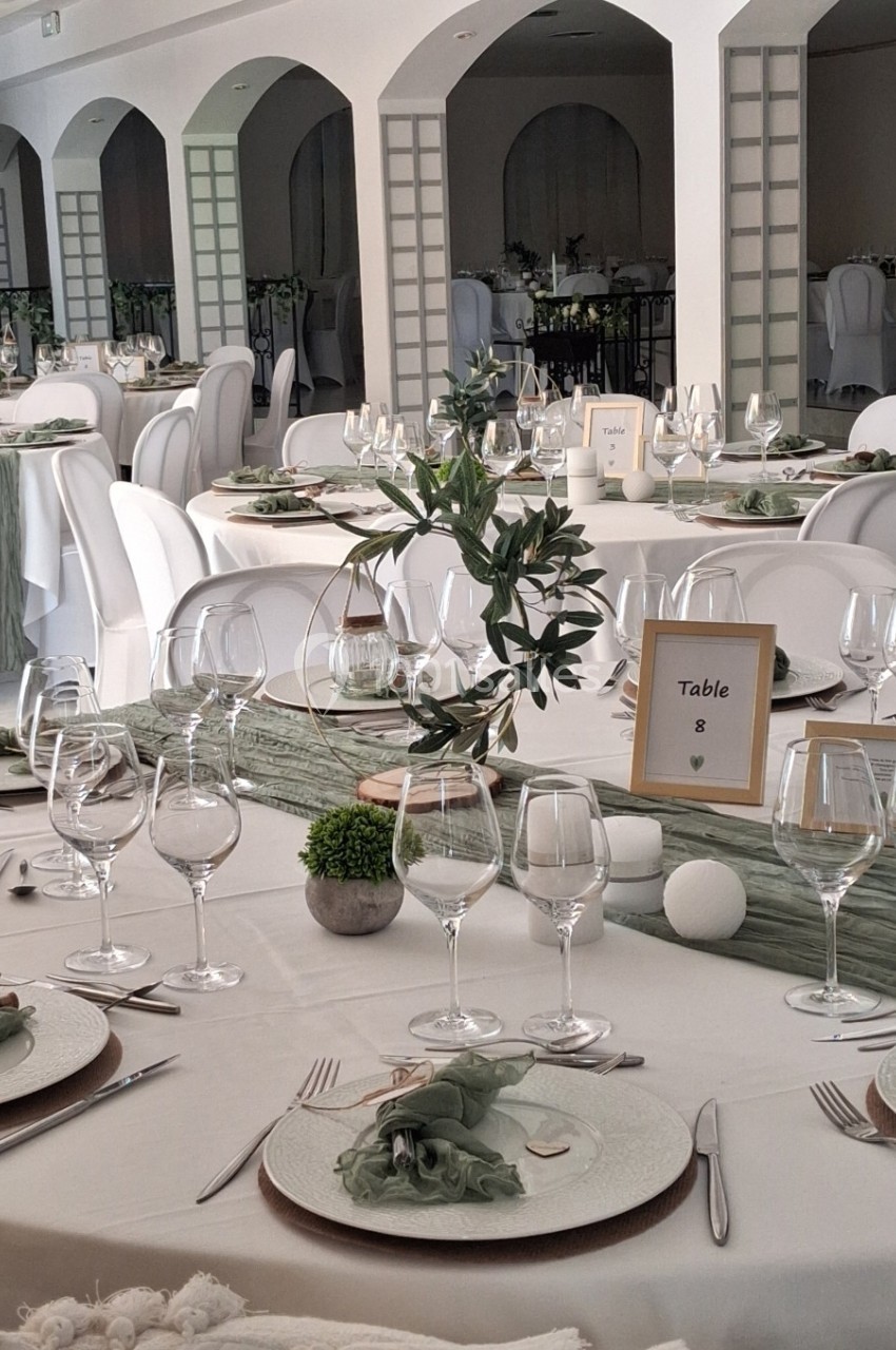 Salle de réception élégamment décorée avec des tables dressées, ornées de centres de table végétaux et de vaisselle raffinée.