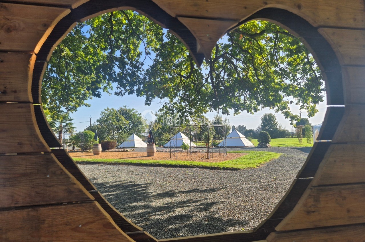 Vue de tentes blanches dans un espace extérieur, encadrée par une découpe en forme de cœur dans une structure en bois.