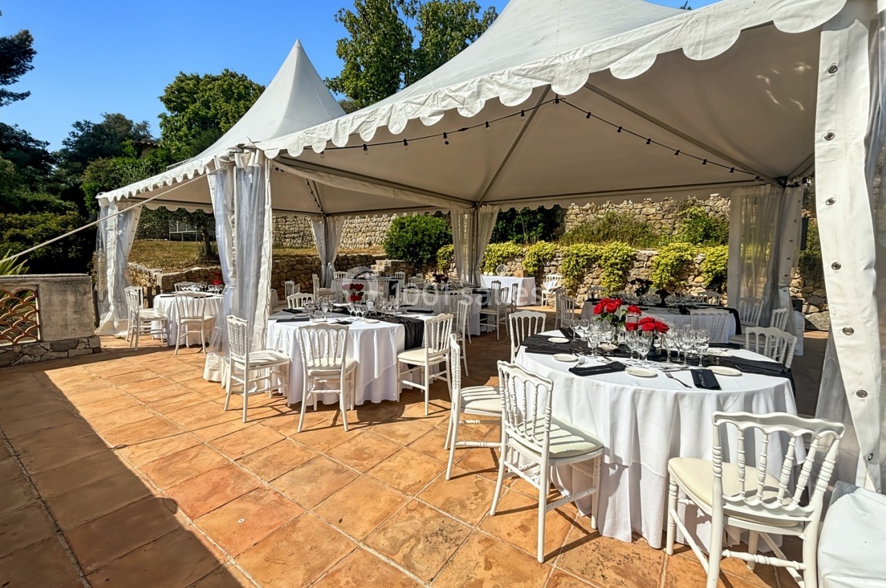 Tentes blanches installées sur une terrasse ensoleillée avec des tables rondes dressées pour un événement.