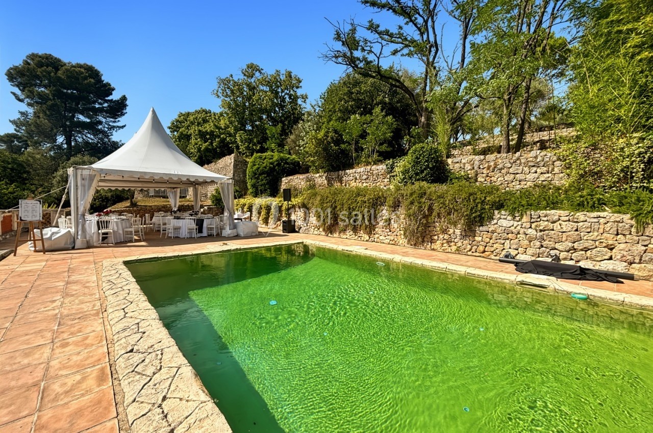 Piscine extérieure entourée de pierres et de végétation, avec une tente blanche aménagée en arrière-plan.