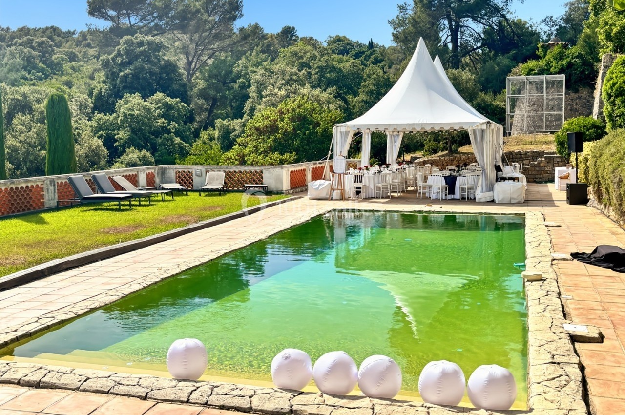 Piscine extérieure entourée de verdure avec une tente blanche aménagée pour un événement sur le côté.