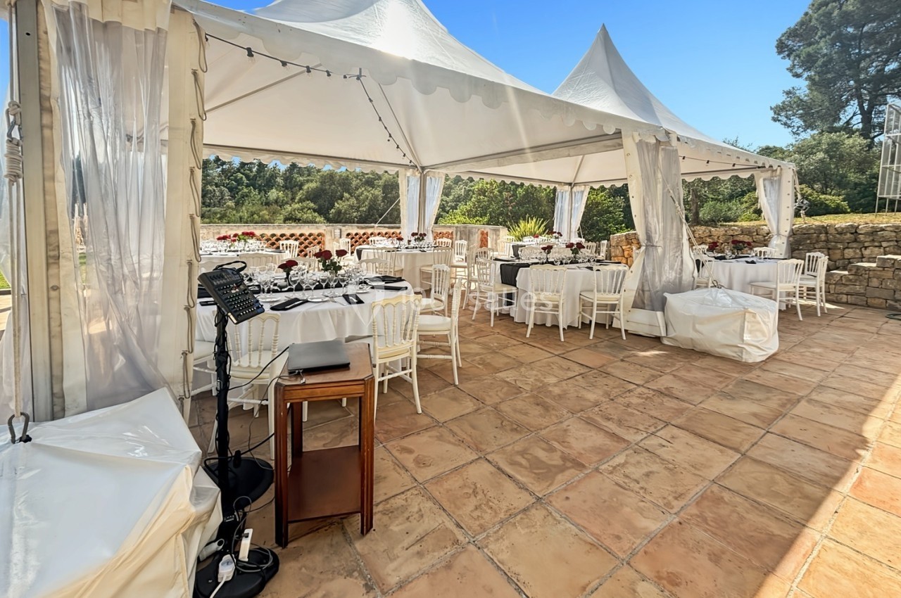 Tente blanche installée en extérieur avec des tables dressées pour un événement, entourée de verdure et de murs en pierre.