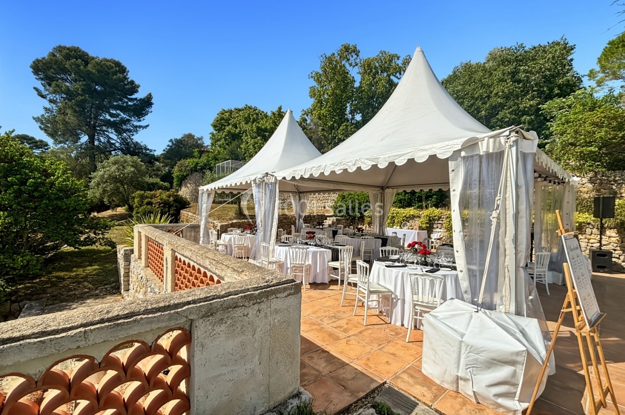 Tentes blanches installées sur une terrasse ensoleillée, avec des tables dressées pour un événement en plein air.