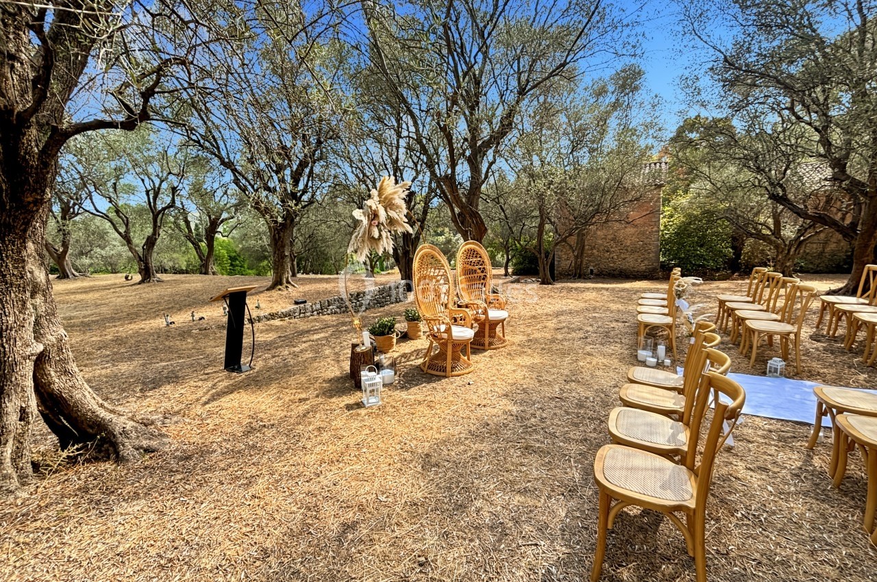 Chaises en bois disposées en extérieur pour une cérémonie, avec deux fauteuils en rotin devant un décor floral.