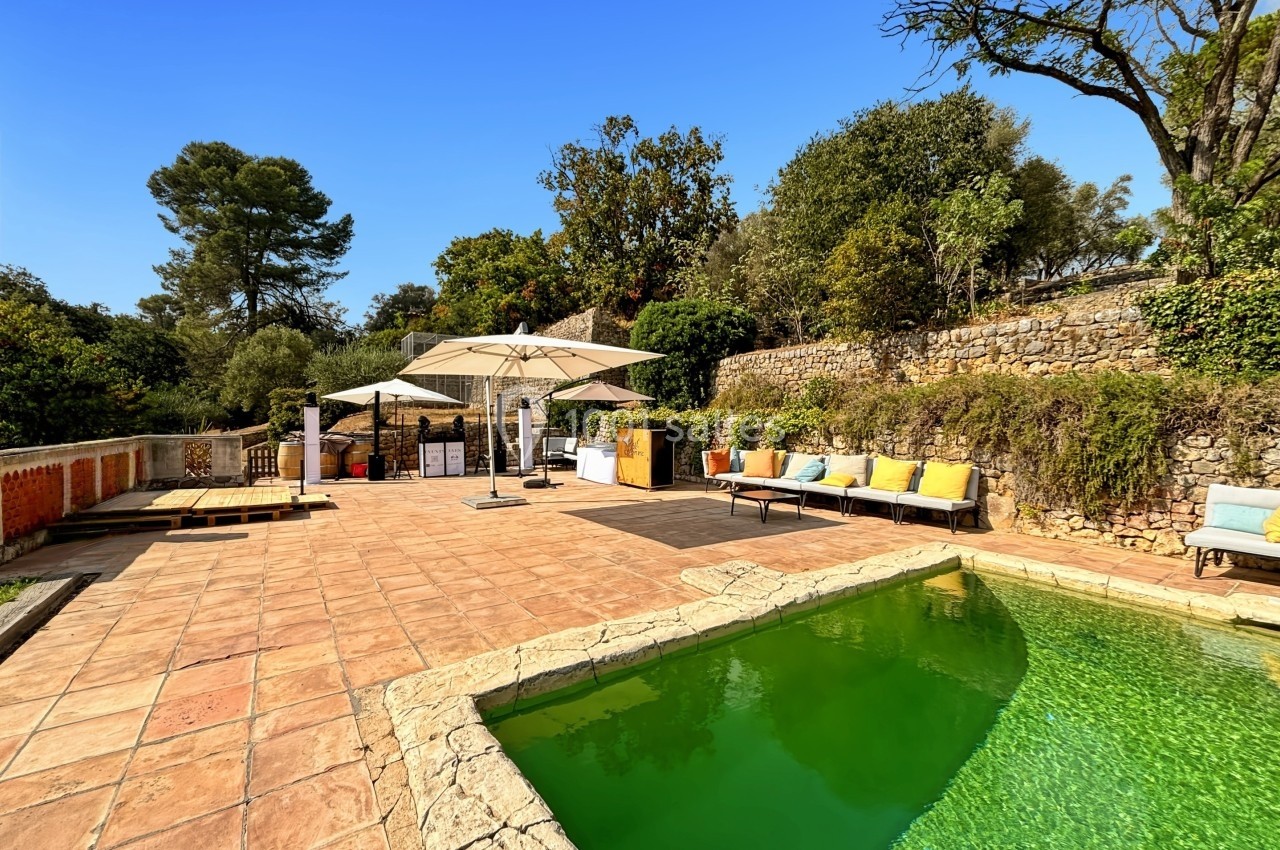 Terrasse ensoleillée avec piscine, transats colorés, parasols et végétation méditerranéenne en arrière-plan.
