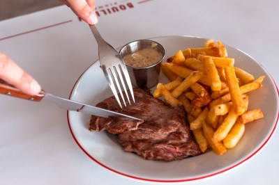 Poulet rôti garni de tranches d'oignon servi dans une assiette, une main utilise une fourchette pour le déguster.