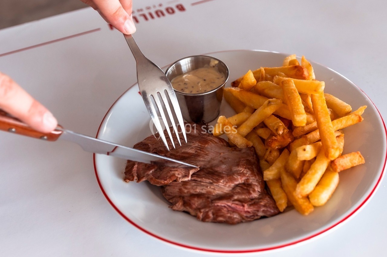 Assiette contenant un steak, des frites dorées et une sauce servie dans un ramequin en métal.