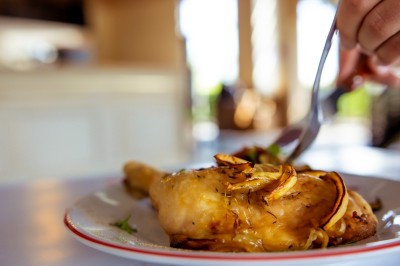 Poulet rôti garni de tranches d'oignon servi dans une assiette, une main utilise une fourchette pour le déguster.