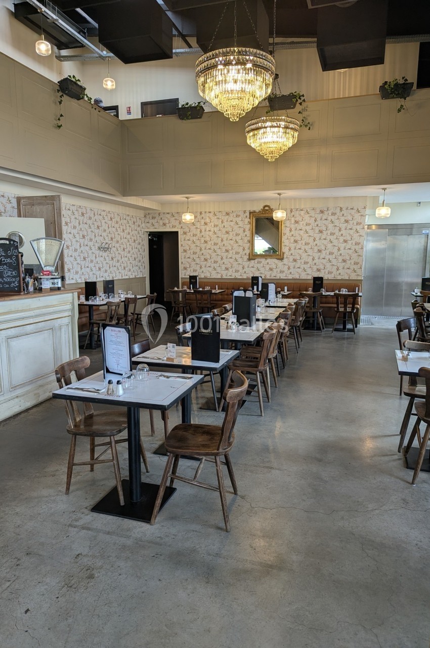 Salle de restaurant lumineuse avec tables en bois, chaises assorties, lustres suspendus et décorations murales.