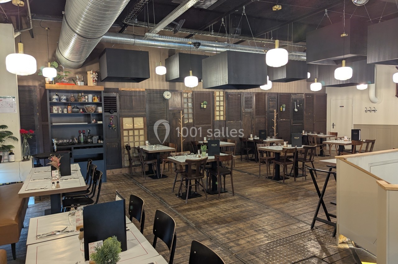 Salle de restaurant moderne avec tables dressées, éclairage suspendu et décoration industrielle.