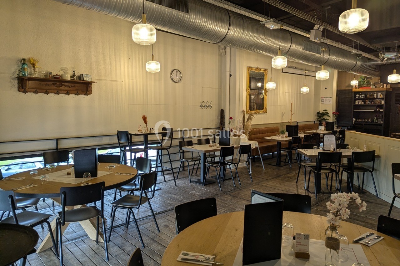 Salle de restaurant lumineuse avec tables en bois, chaises noires, décorations murales et suspensions modernes.