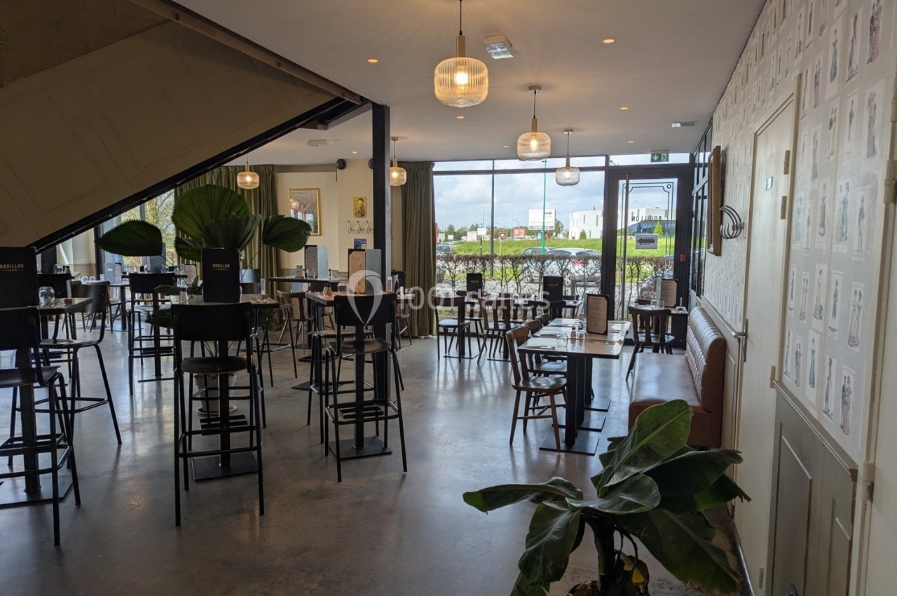 Salle de restaurant lumineuse avec des tables et chaises en bois, grandes fenêtres donnant sur un extérieur verdoyant.