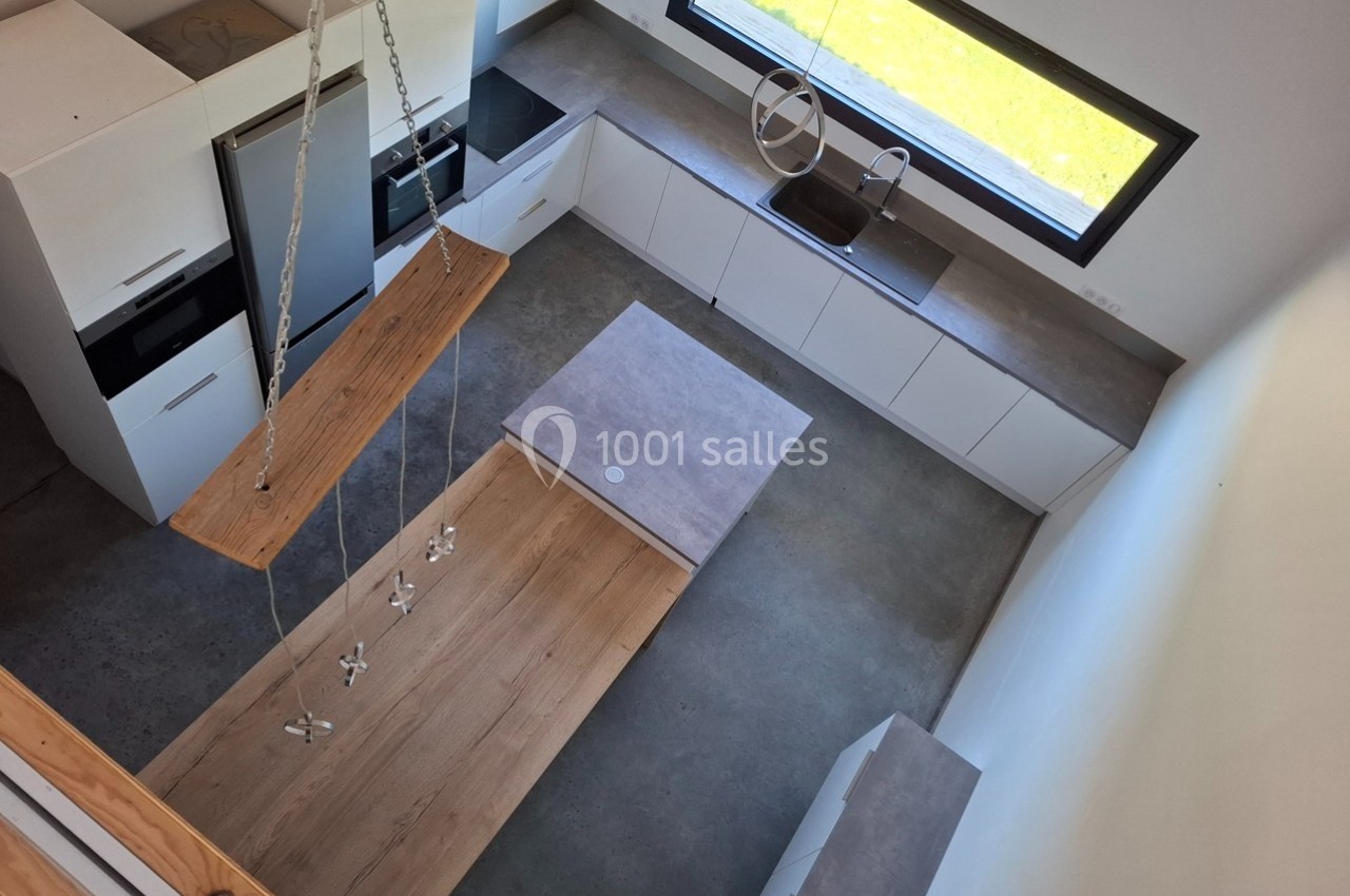Cuisine moderne vue de dessus avec îlot central, plancher en bois, mobilier blanc et grande fenêtre apportant de la lumière.